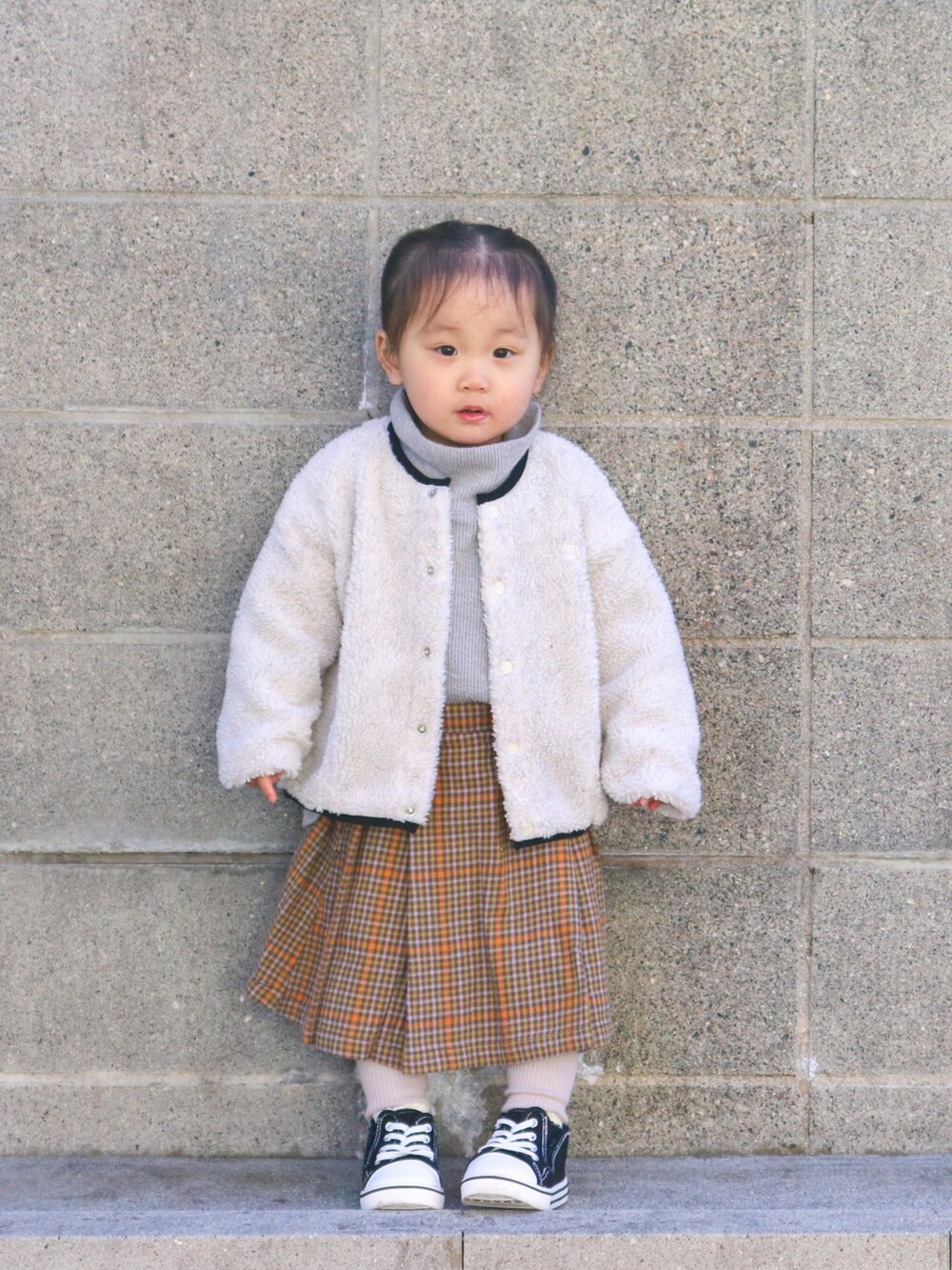 ホワイト系のノーカラージャケット、グレー系のTシャツ/カットソー、ブラウン系のスカートを着用したキッズの冬コーディネートの2枚目の写真