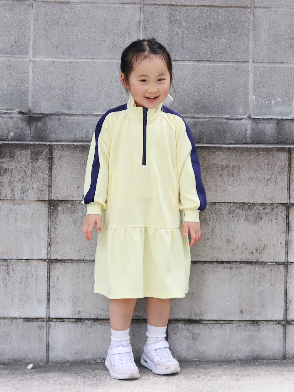 イエロー系のワンピース、ピンク系のスニーカー、ホワイト系のソックス/靴下を着用したキッズの冬コーディネートの2枚目の写真