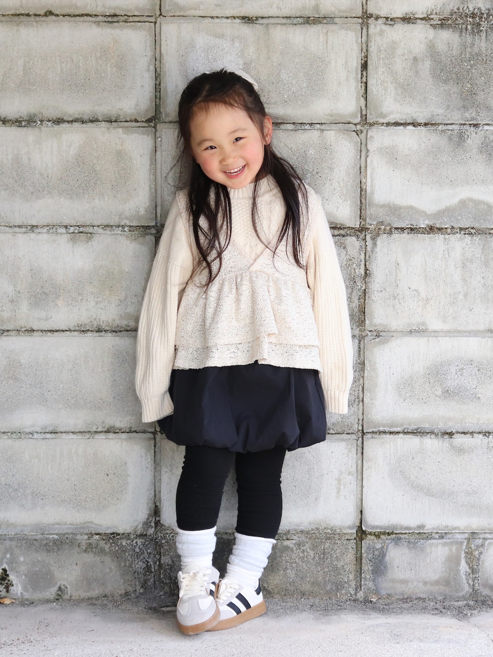 ホワイト系のニット/セーター、ベージュ系のベスト、ブラック系のスカートを着用したキッズの冬コーディネートの2枚目の写真