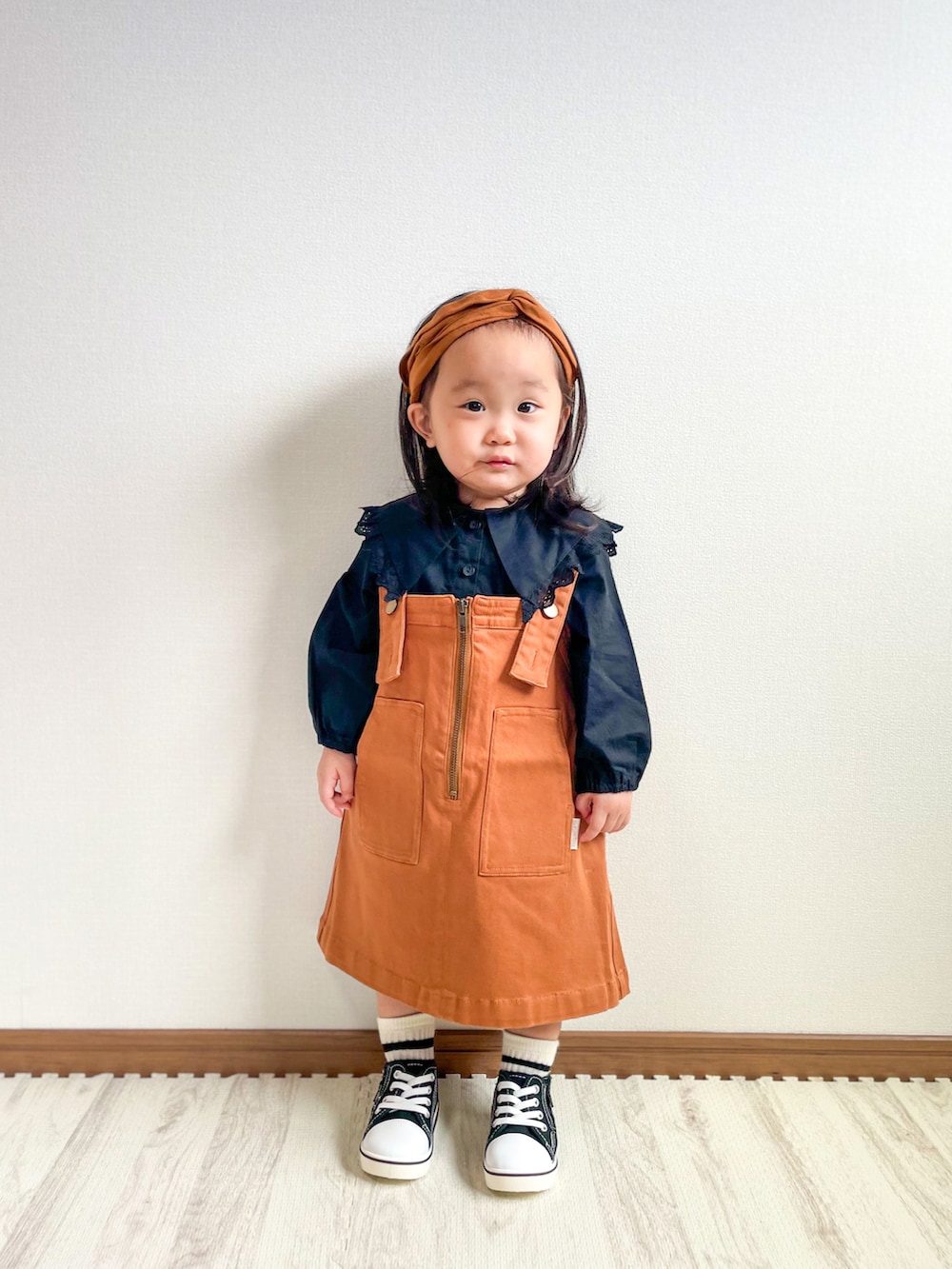 ブラック系のシャツ/ブラウス、イエロー系のジャンパースカート、ブラック系のスニーカーを着用したキッズの秋コーディネートの2枚目の写真