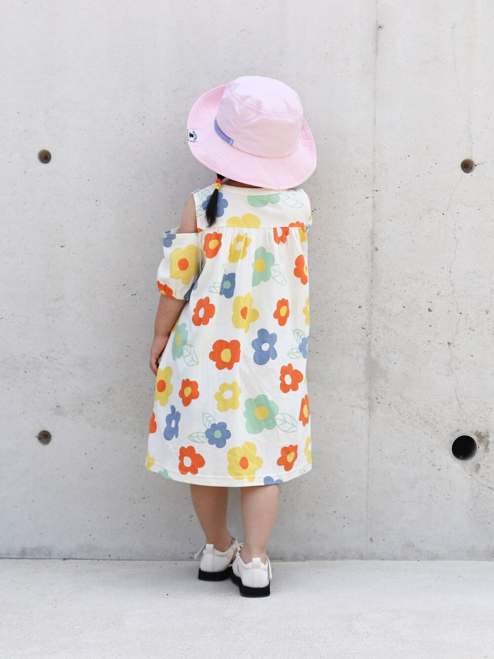 オレンジ系のワンピース、ホワイト系のサンダル、ピンク系のハットを着用したキッズの夏コーディネートの3枚目の写真
