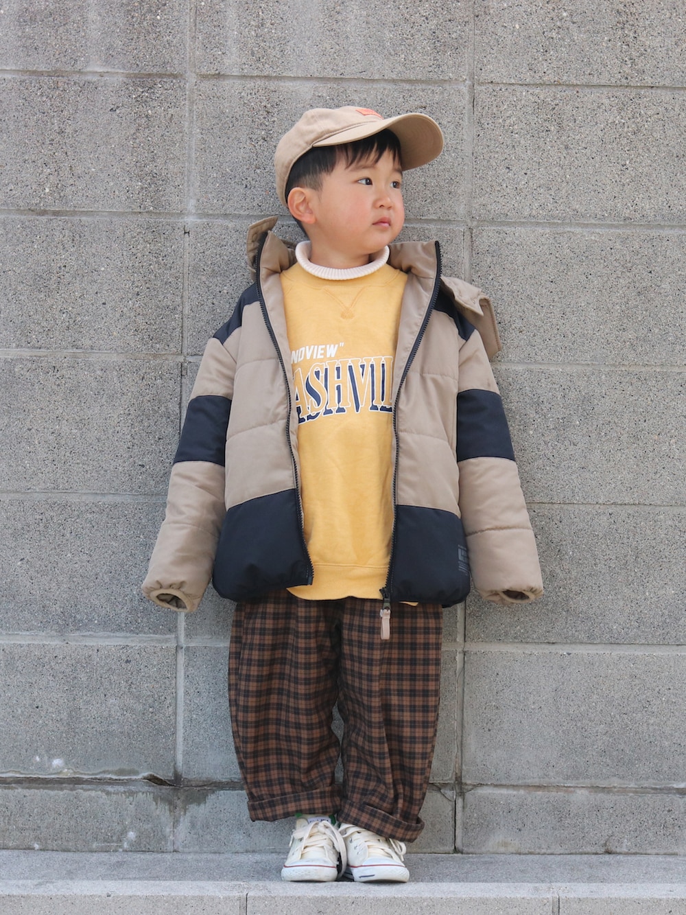 ベージュ系のダウンジャケット/コート、イエロー系のスウェット、ホワイト系のニット/セーターを着用したキッズの冬コーディネートの2枚目の写真