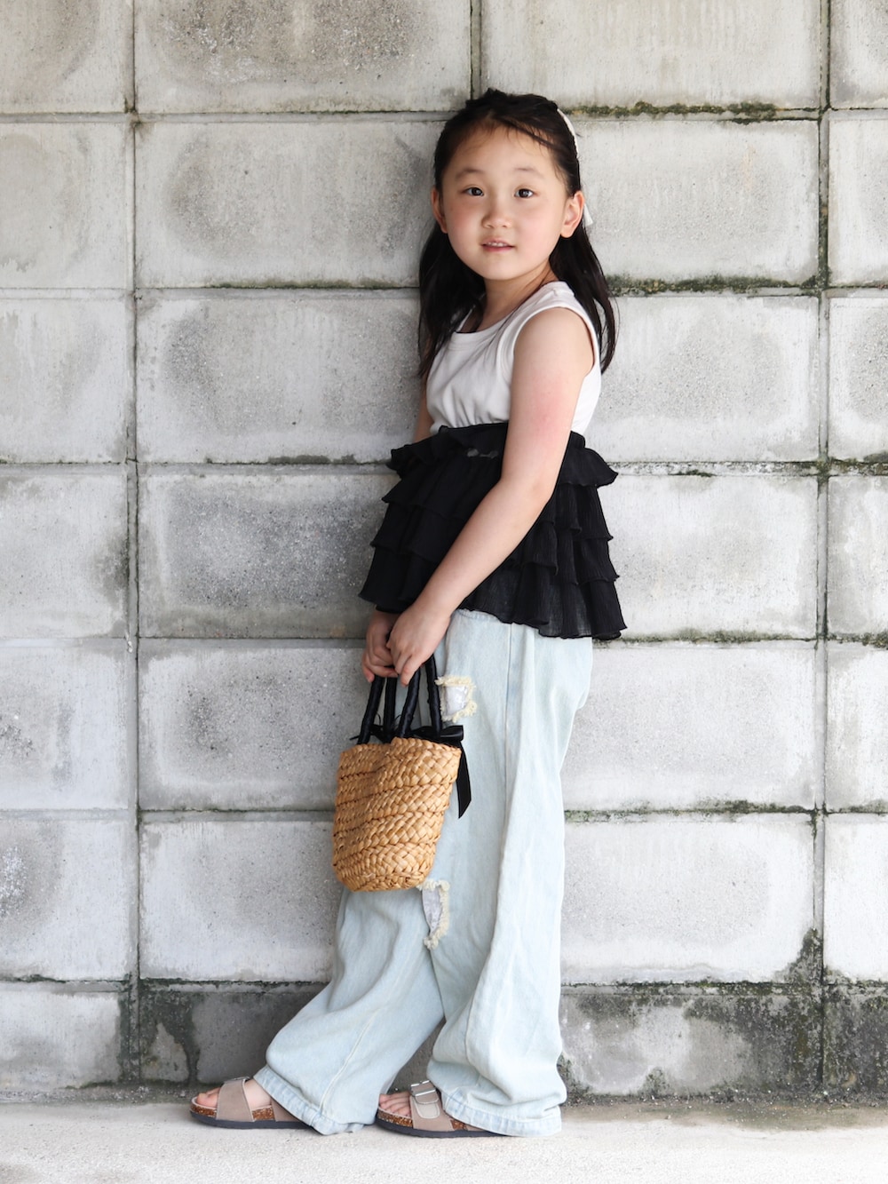 ブルー系のデニムパンツ、ブラック系のかごバッグ、ベージュ系のサンダルを着用したキッズの夏コーディネートの2枚目の写真