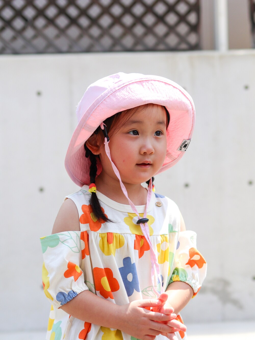 オレンジ系のワンピース、ホワイト系のサンダル、ピンク系のハットを着用したキッズの夏コーディネートの4枚目の写真