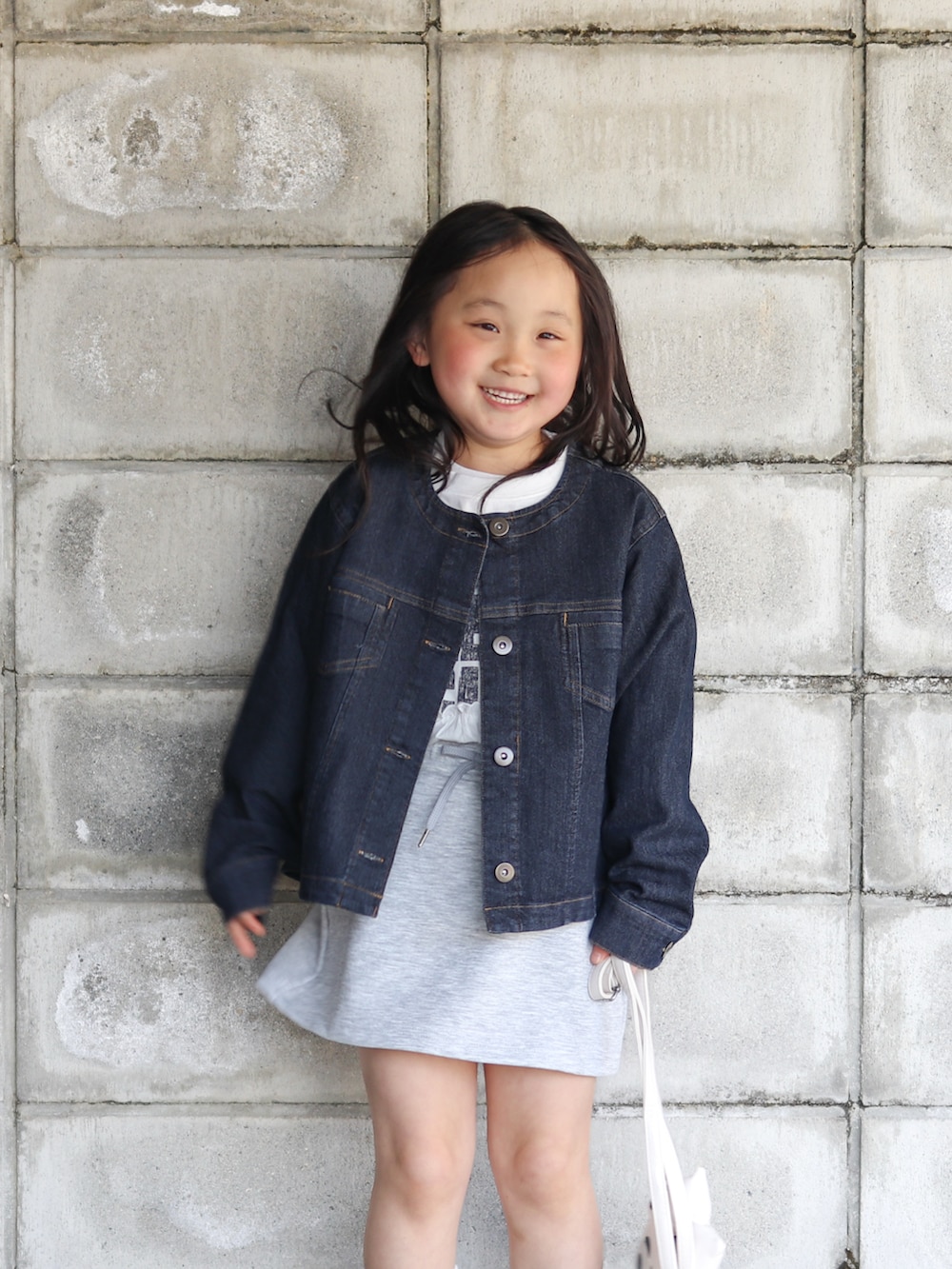 ブルー系のブルゾン、ホワイト系のワンピース、ホワイト系のショルダーバッグを着用したキッズの春コーディネートの2枚目の写真