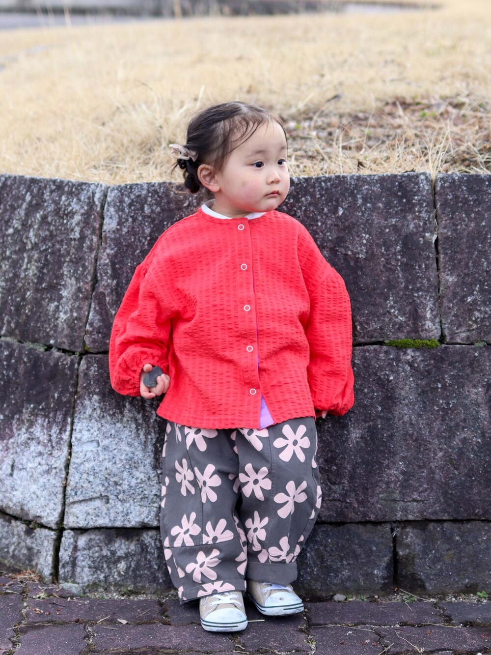 レッド系のカーディガン/ボレロ、グレー系のスラックス、ベージュ系のスニーカーを着用したキッズの春コーディネートの2枚目の写真