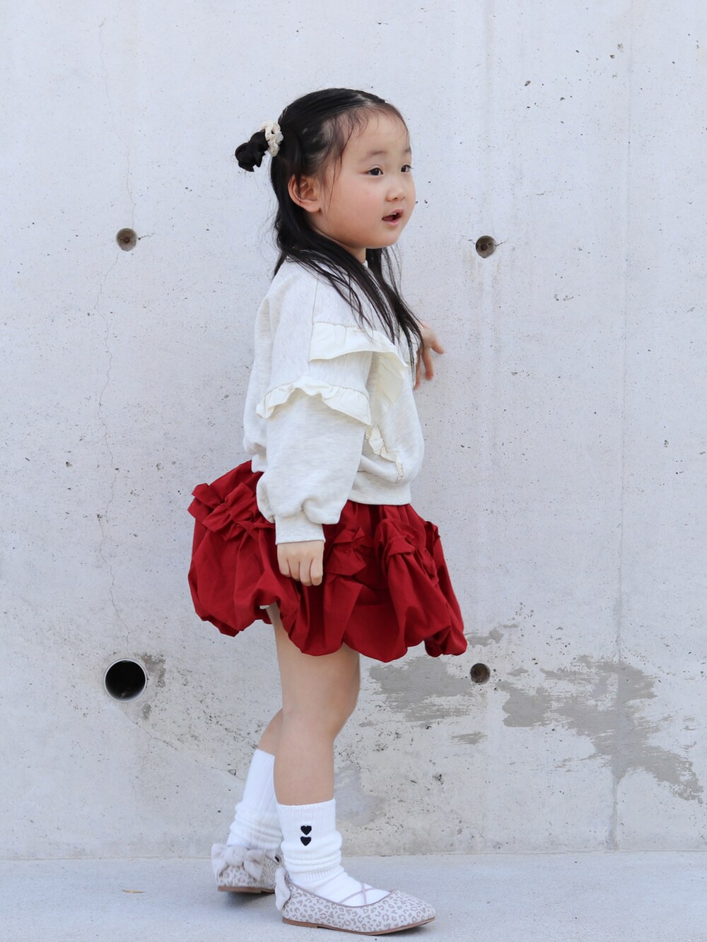 ベージュ系のスウェット、レッド系のスカート、ベージュ系のバレエシューズを着用したキッズの秋コーディネートの3枚目の写真