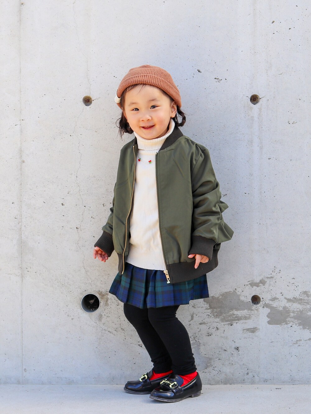 グリーン系のMA-1、ホワイト系のニット/セーター、グリーン系のスカートを着用したキッズの秋コーディネートの3枚目の写真