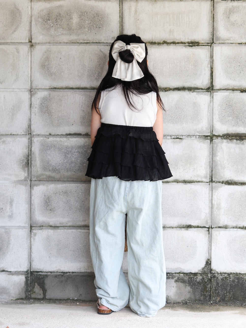 ブルー系のデニムパンツ、ブラック系のかごバッグ、ベージュ系のサンダルを着用したキッズの夏コーディネートの3枚目の写真