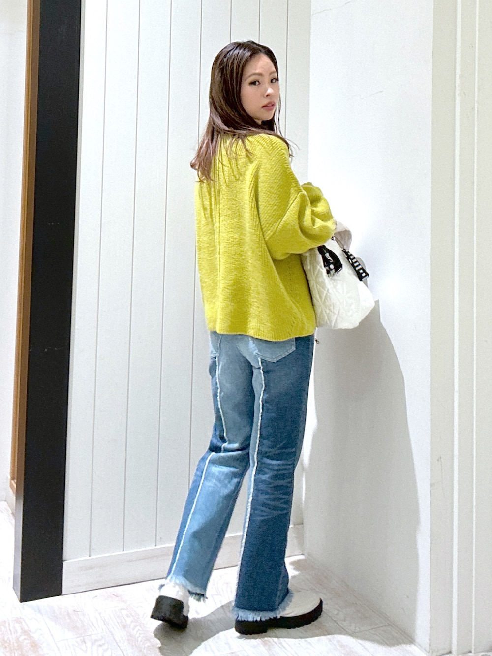 シルバー系のトートバッグ、ベージュ系のブーツ、イエロー系のニット/セーターを着用したレディースの冬コーディネートの3枚目の写真