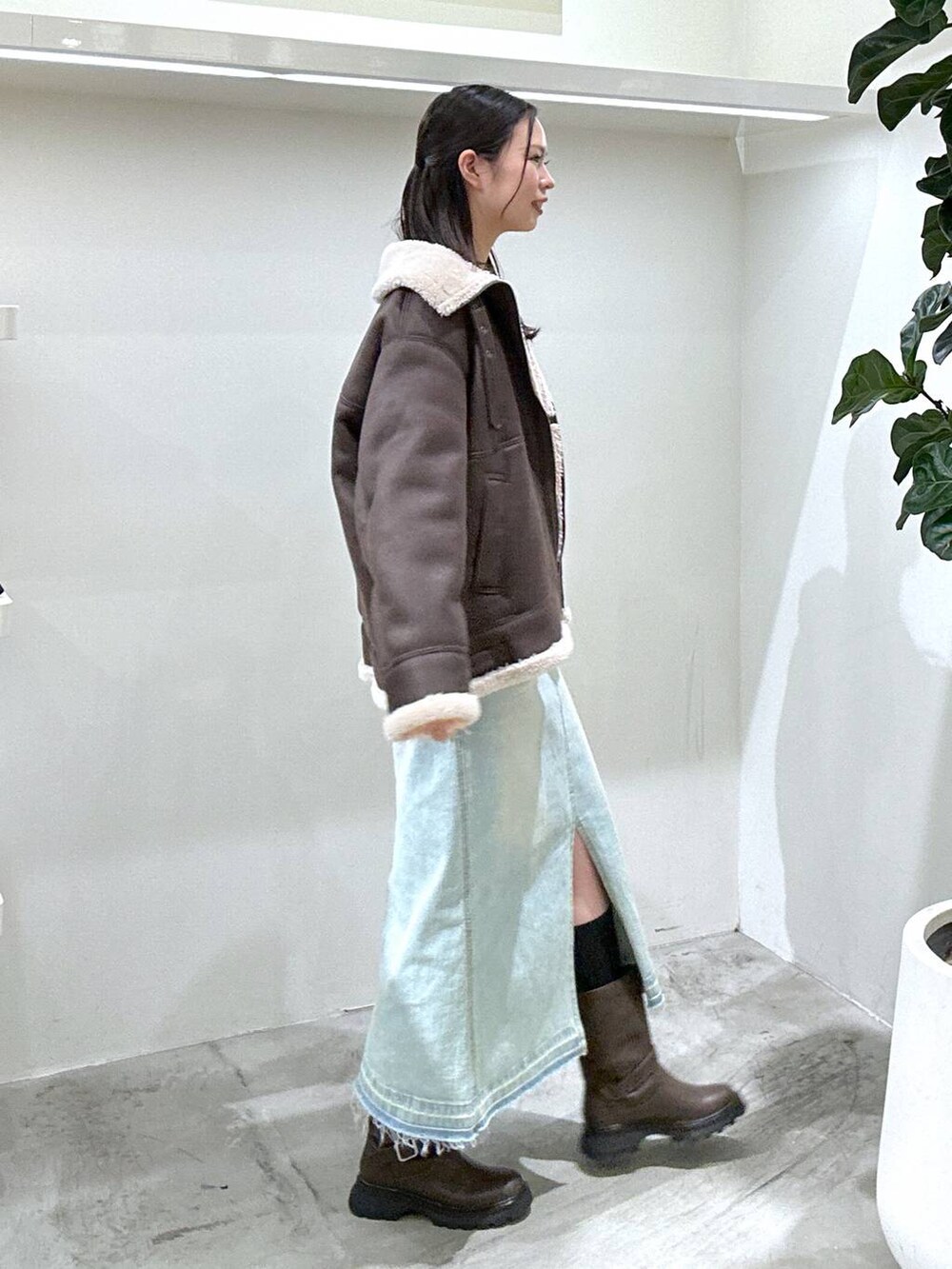 ブルー系のデニムスカート、ブラウン系のブーツ、シルバー系のショルダーバッグを着用したレディースの冬コーディネートの2枚目の写真