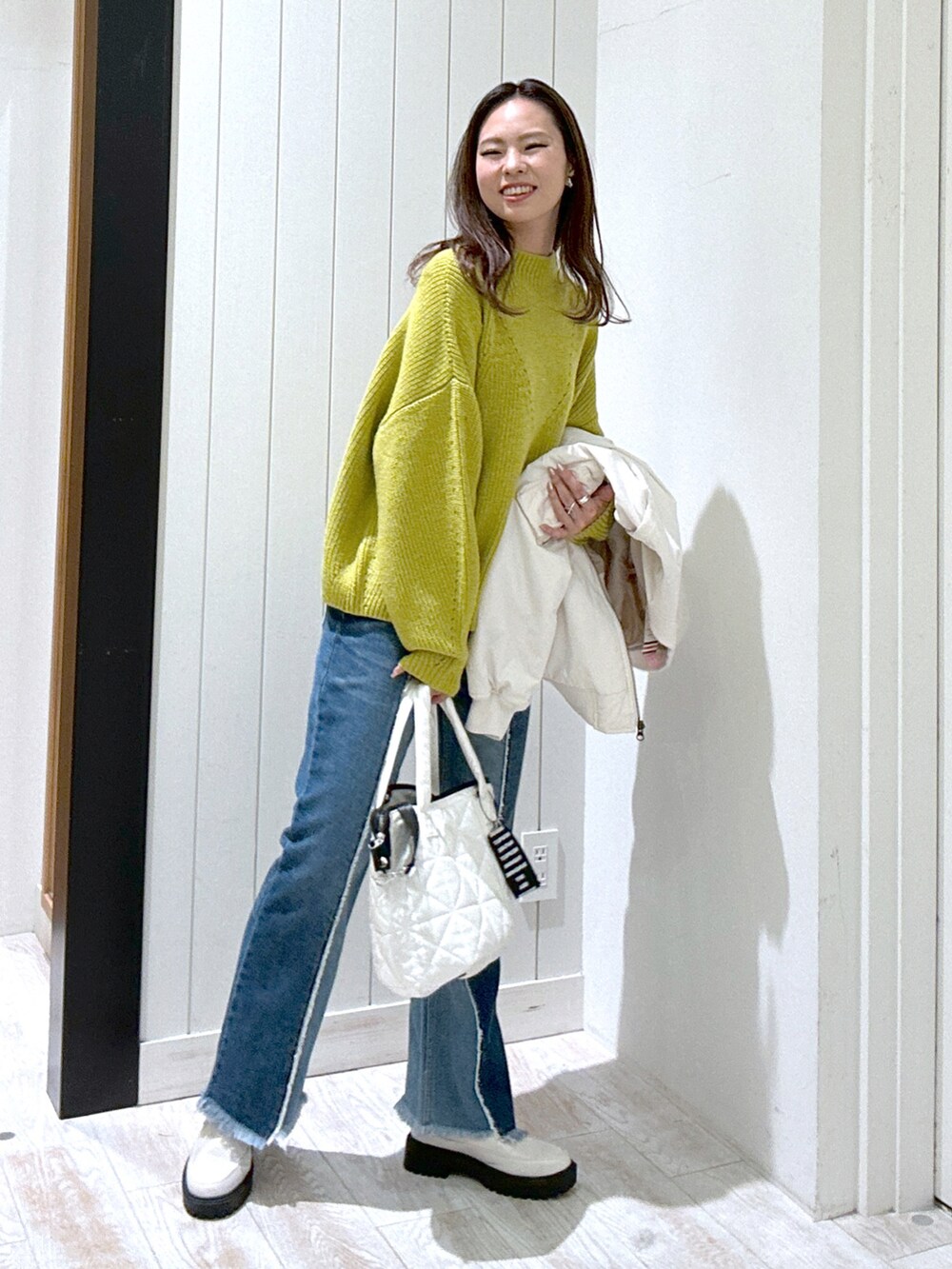 シルバー系のトートバッグ、ベージュ系のブーツ、イエロー系のニット/セーターを着用したレディースの冬コーディネートの2枚目の写真