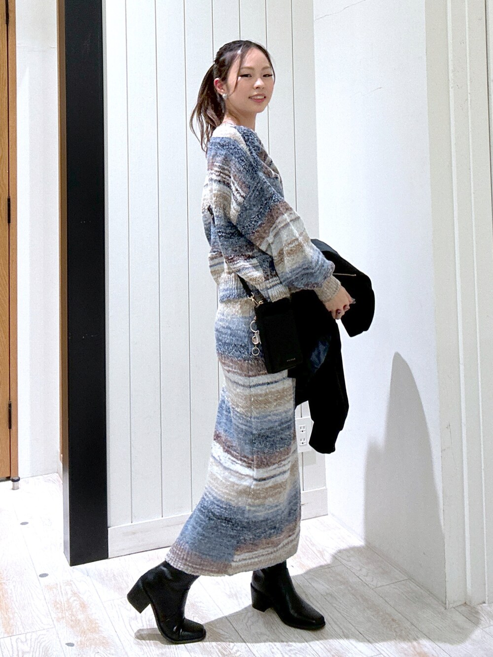 ブルー系のニット/セーター、ブラック系のバッグ、ブルー系のスカートを着用したレディースの秋コーディネートの3枚目の写真