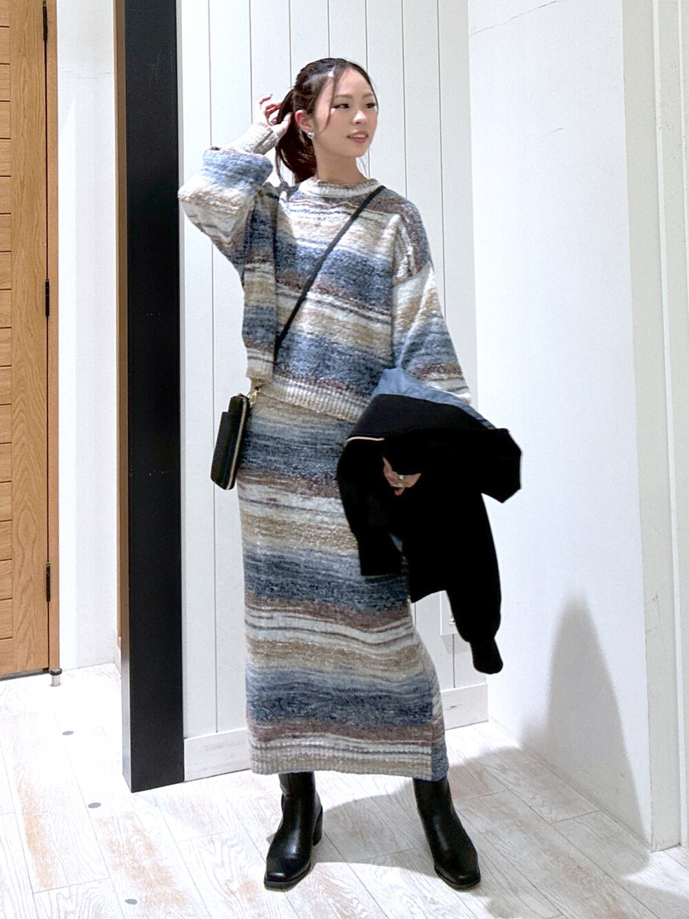 ブルー系のニット/セーター、ブラック系のバッグ、ブルー系のスカートを着用したレディースの秋コーディネートの2枚目の写真