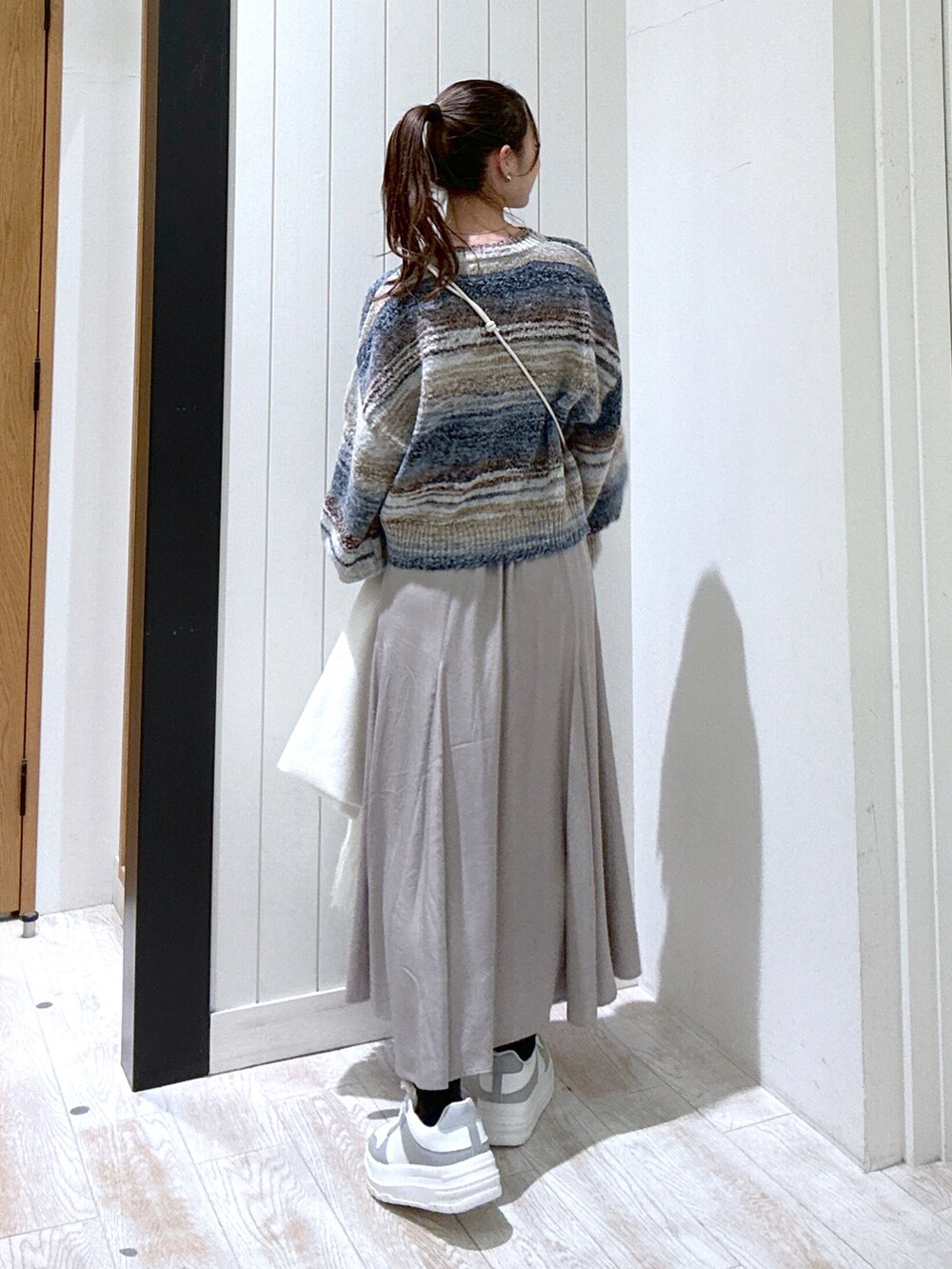ブルー系のニット/セーター、ベージュ系のショルダーバッグ、ベージュ系のスカートを着用したレディースの秋コーディネートの3枚目の写真