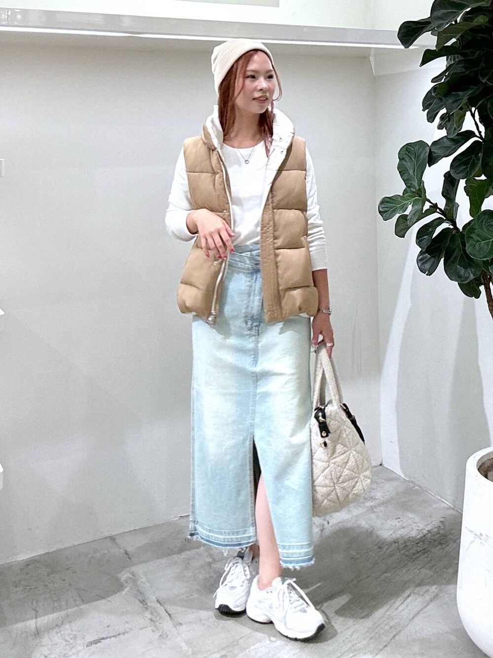 グレー系のスニーカー、ブルー系のデニムスカート、ブラウン系のベストを着用したレディースの秋コーディネートの2枚目の写真