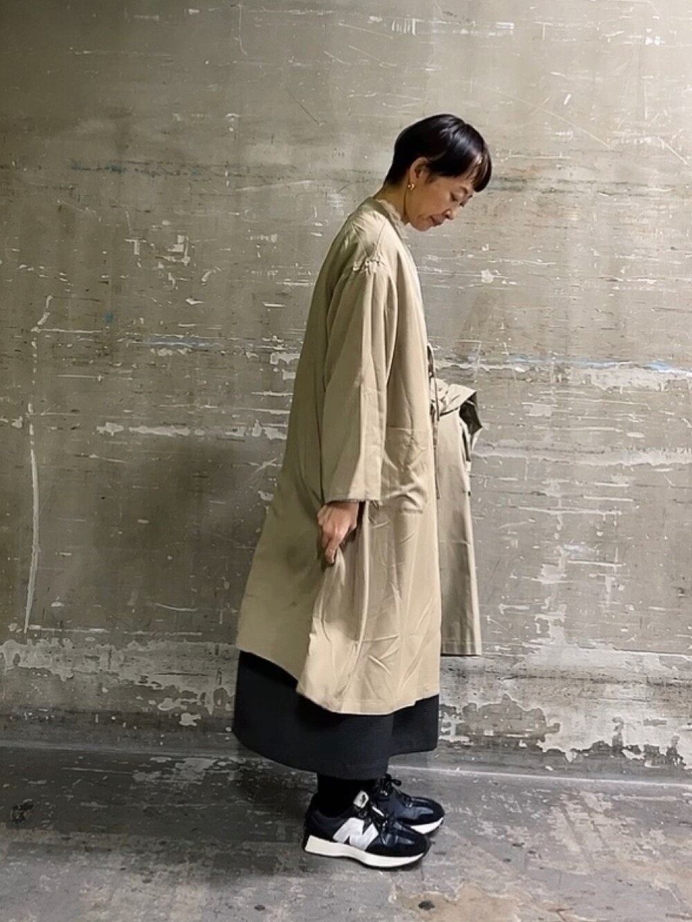 ベージュ系のノーカラーコート、ホワイト系のTシャツ/カットソー、ブラック系のワンピースを着用したレディースの冬コーディネートの2枚目の写真