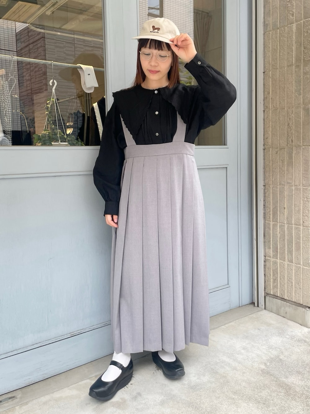 ブラック系のシャツ/ブラウス、グレー系のジャンパースカート、ベージュ系のキャップを着用したレディースの春コーディネートの2枚目の写真