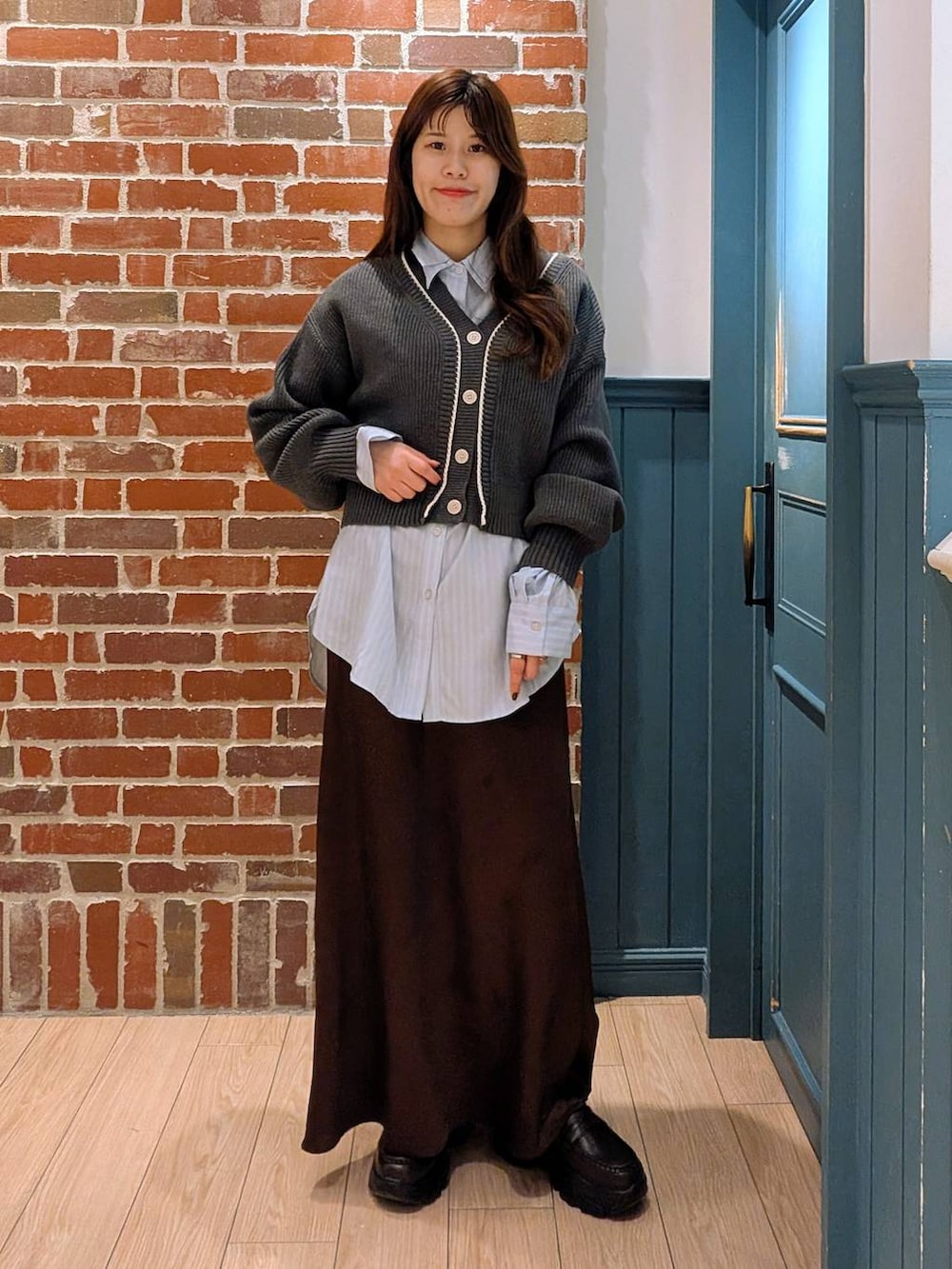 ブラウン系のスカート、グレー系のカーディガン/ボレロ、ブラック系のローファーを着用したレディースの冬コーディネートの2枚目の写真