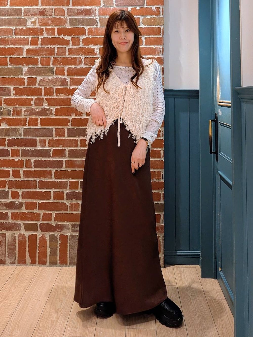 ブラウン系のスカート、ブラック系のローファー、ホワイト系のベストを着用したレディースの冬コーディネートの2枚目の写真