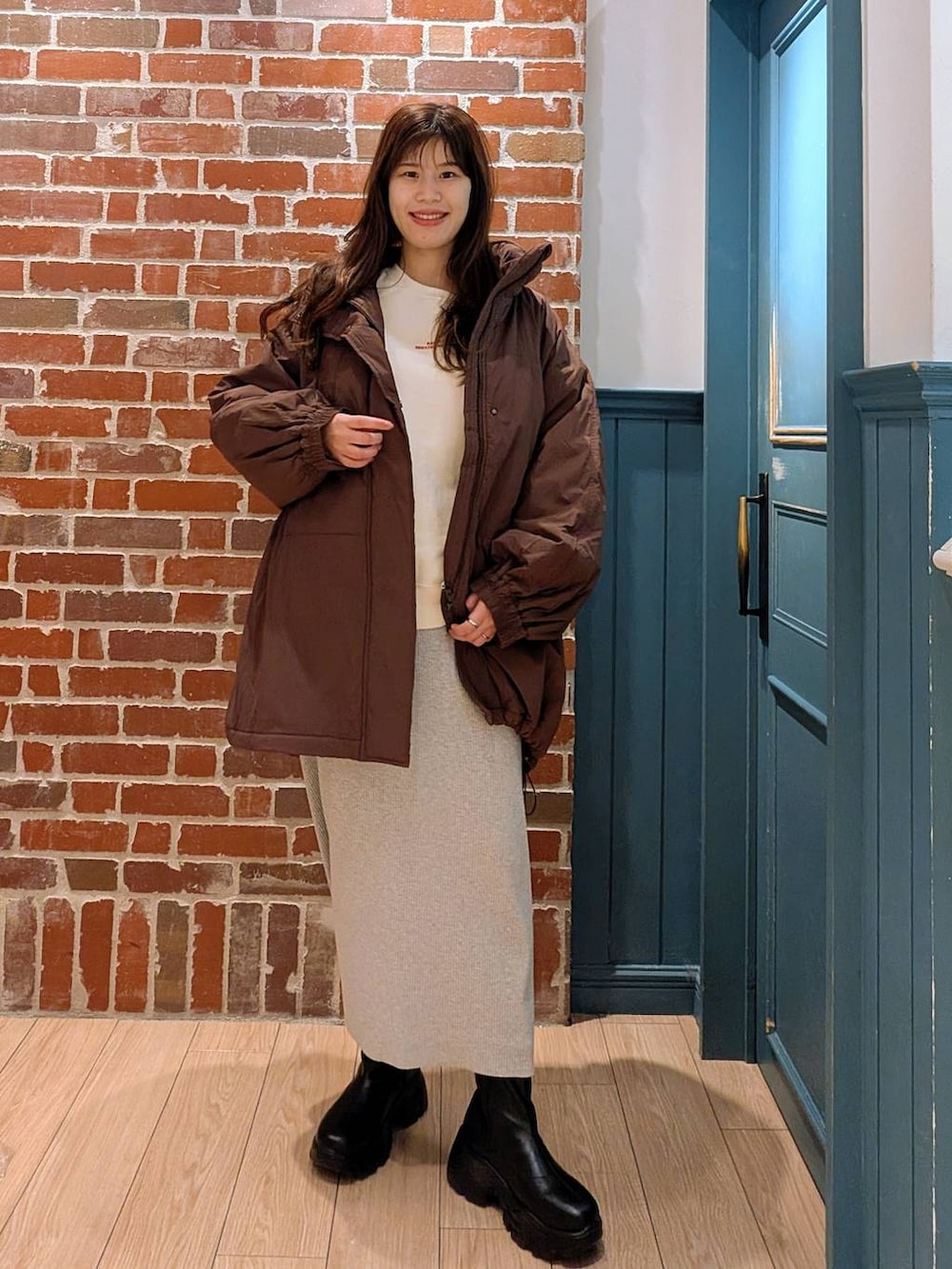 グレー系のスカート、ブラック系のブーツ、ブラウン系のブルゾンを着用したレディースの冬コーディネートの2枚目の写真