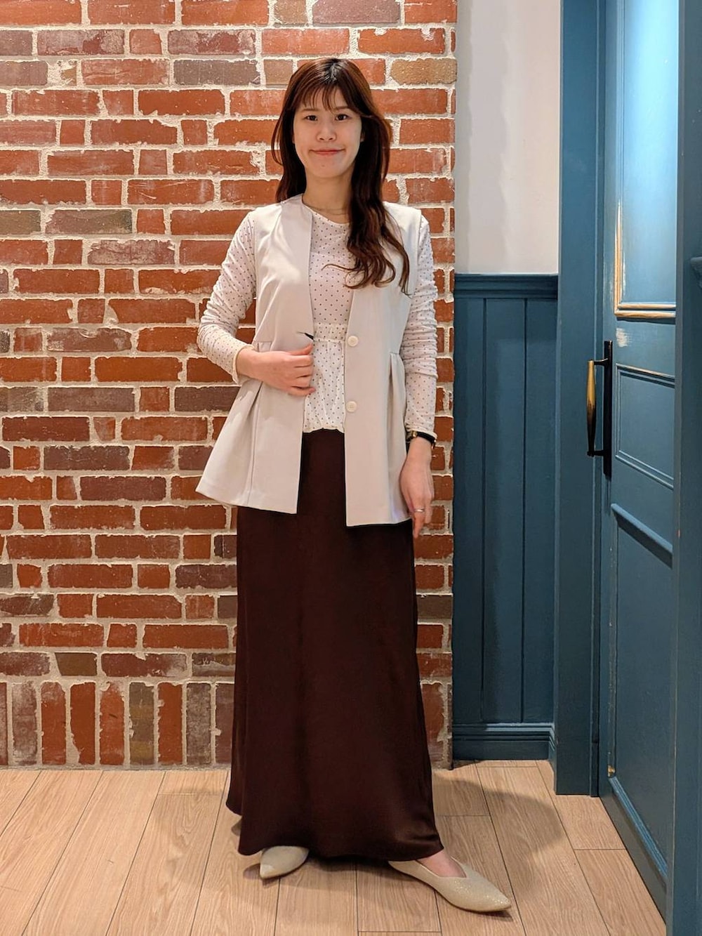 ブラウン系のスカート、ホワイト系のベスト、ホワイト系のパンプスを着用したレディースの春コーディネートの2枚目の写真