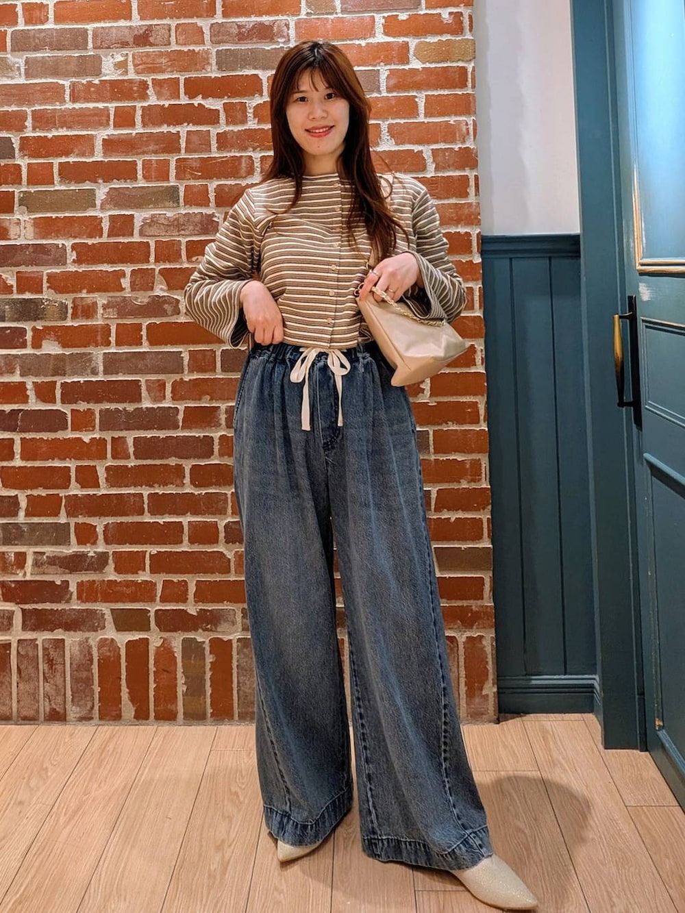 ブルー系のデニムパンツ、ベージュ系のショルダーバッグ、ホワイト系のパンプスを着用したレディースの春コーディネートの2枚目の写真