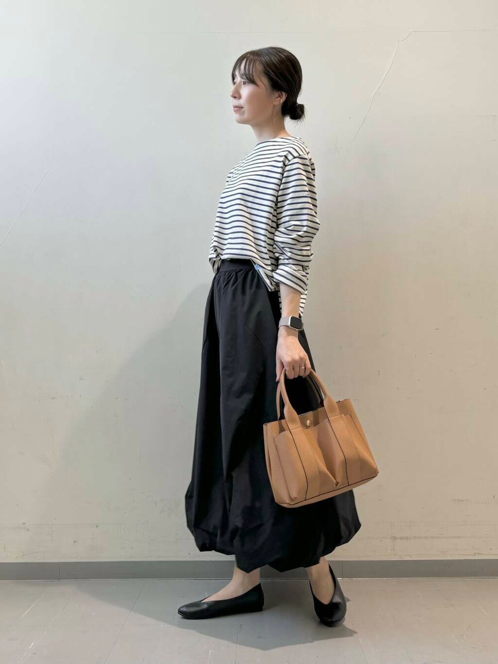 ベージュ系のトートバッグ、ブラック系のパンプス、ブラック系のスカートを着用したレディースの秋コーディネートの3枚目の写真