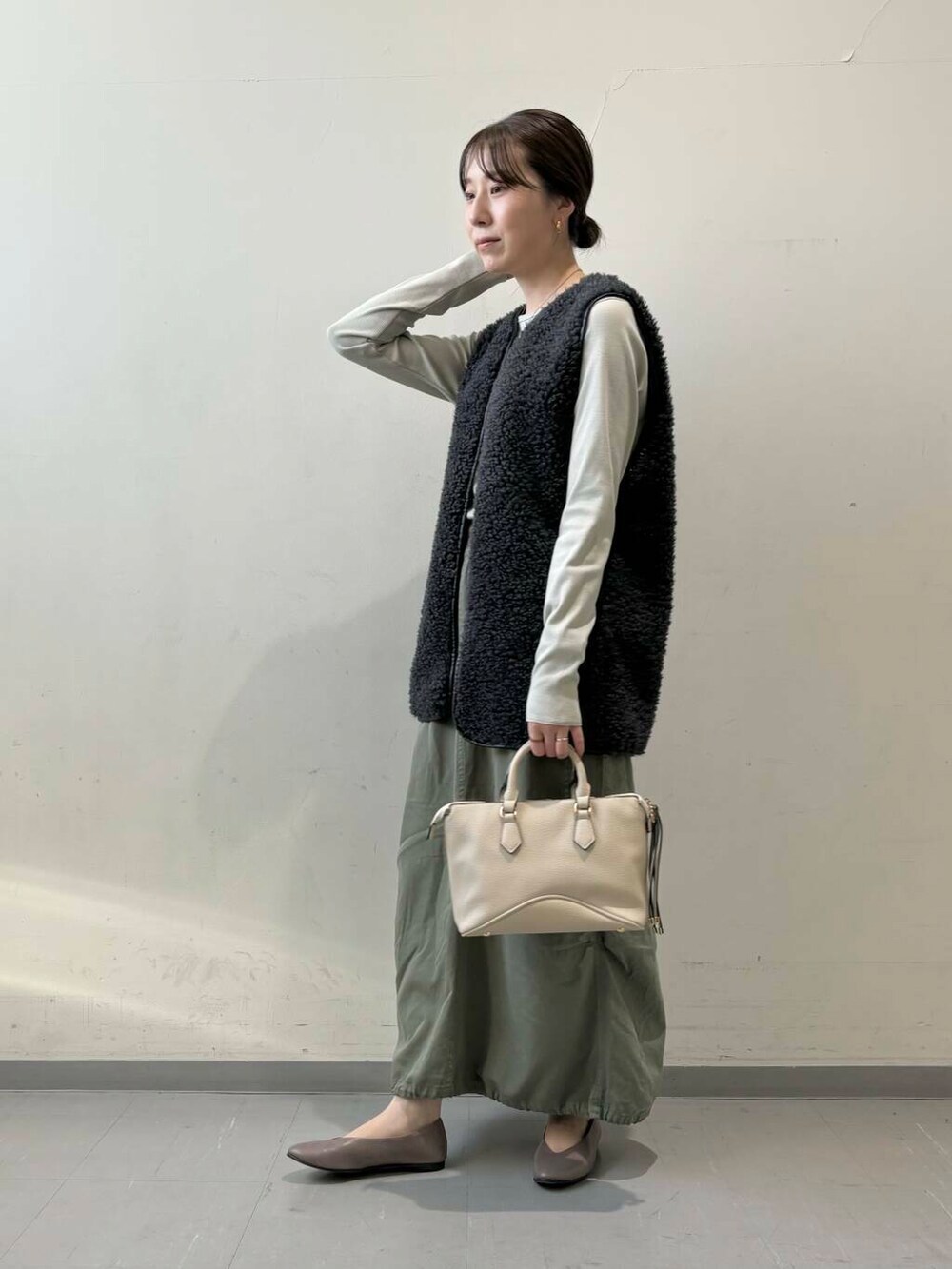 ベージュ系のパンプス、グレー系のベスト、グリーン系のスカートを着用したレディースの秋コーディネートの2枚目の写真