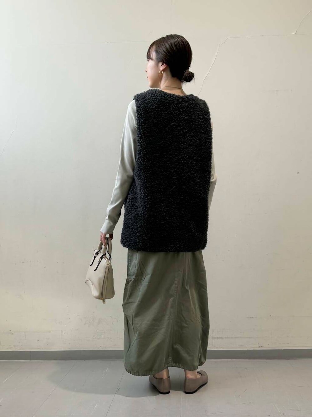 ベージュ系のパンプス、グレー系のベスト、グリーン系のスカートを着用したレディースの秋コーディネートの3枚目の写真