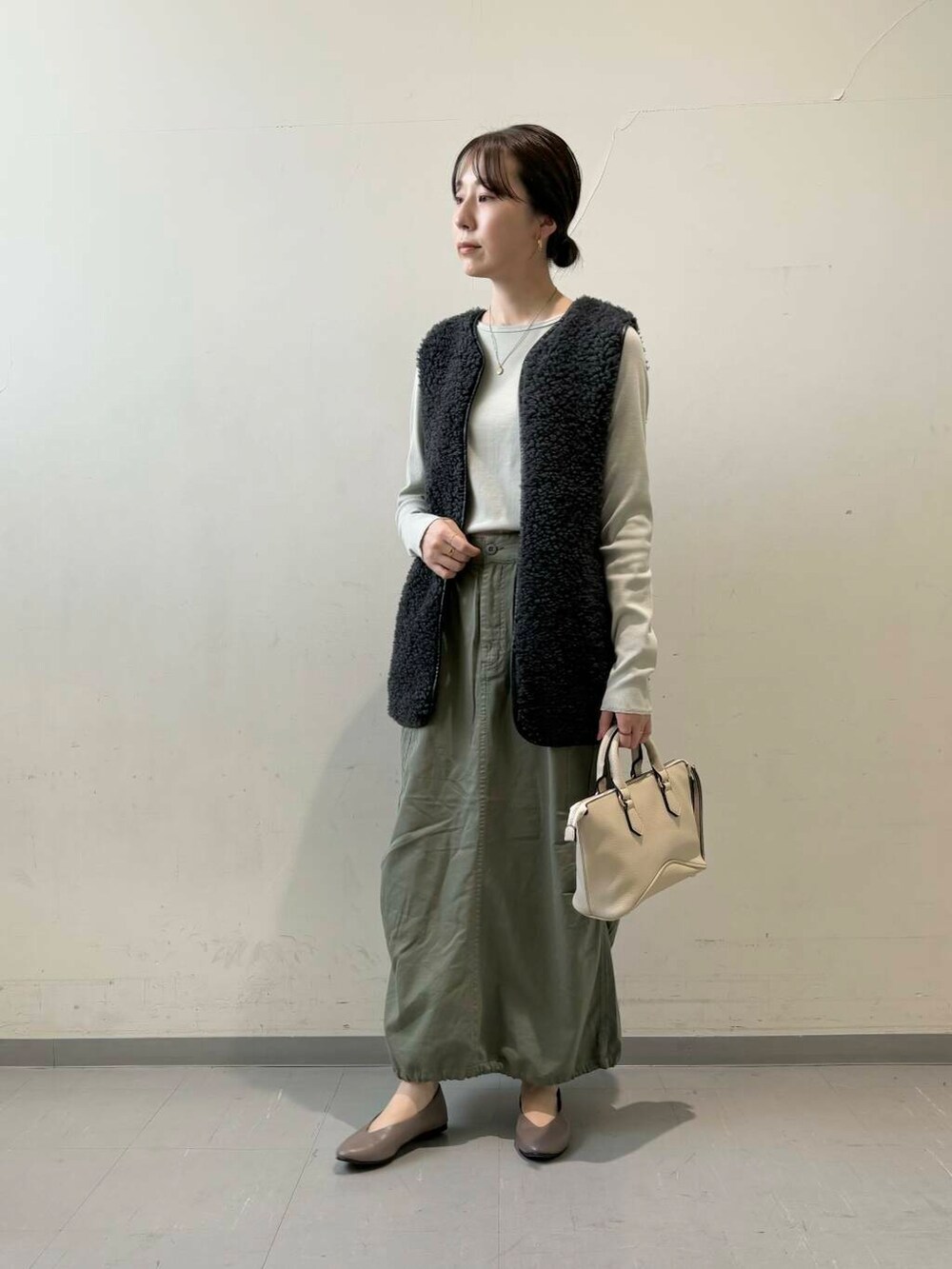 ベージュ系のパンプス、グレー系のベスト、グリーン系のスカートを着用したレディースの秋コーディネートの4枚目の写真