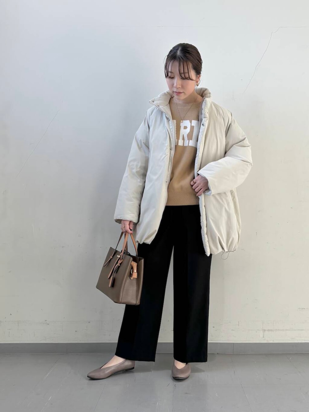 ベージュ系のパンプス、ブラウン系のハンドバッグ、ベージュ系のニット/セーターを着用したレディースの冬コーディネートの2枚目の写真