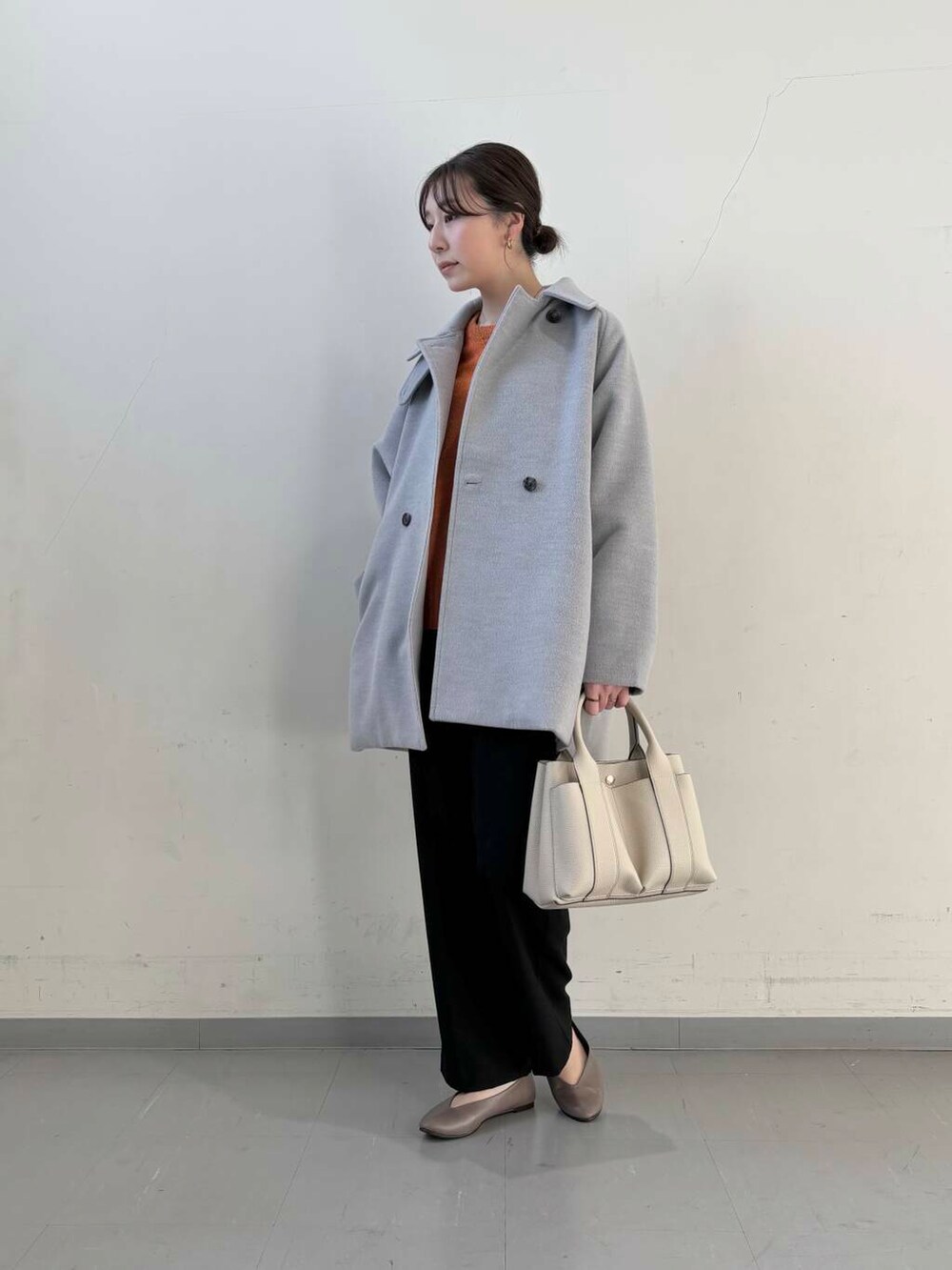 ベージュ系のパンプス、オレンジ系のニット/セーター、グレー系のステンカラーコートを着用したレディースの冬コーディネートの2枚目の写真