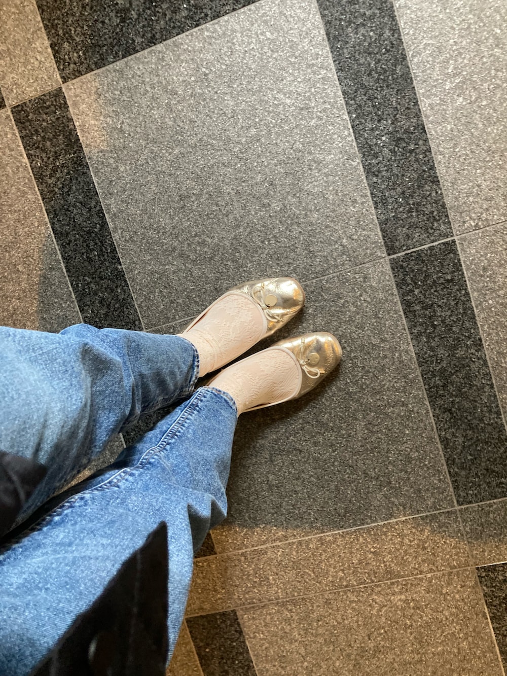 ブラック系のデニムパンツ、ゴールド系のバレエシューズ、ホワイト系のレッグウェアを着用したレディースの春コーディネートの2枚目の写真