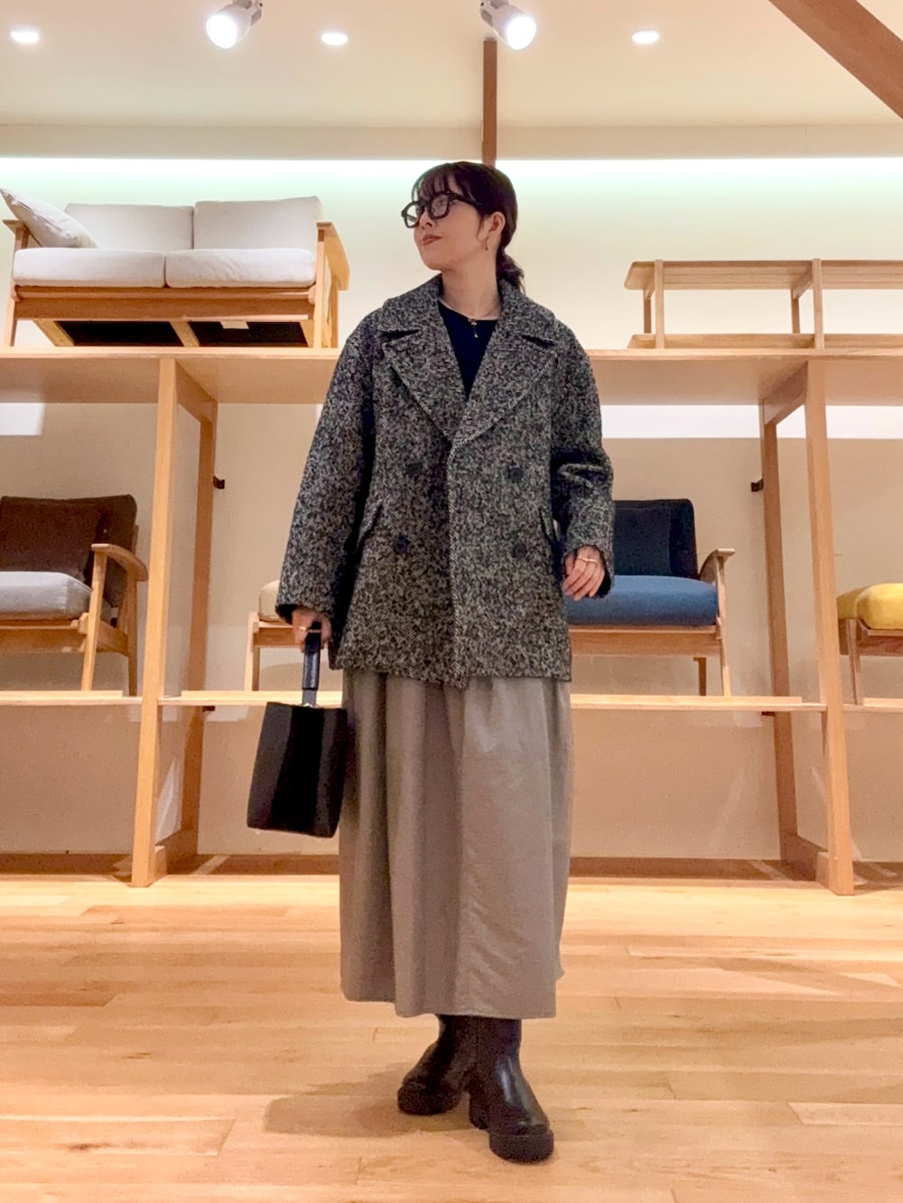 ブラック系のピーコート、ブラック系のハンドバッグ、ブルー系のニット/セーターを着用したレディースの冬コーディネートの2枚目の写真