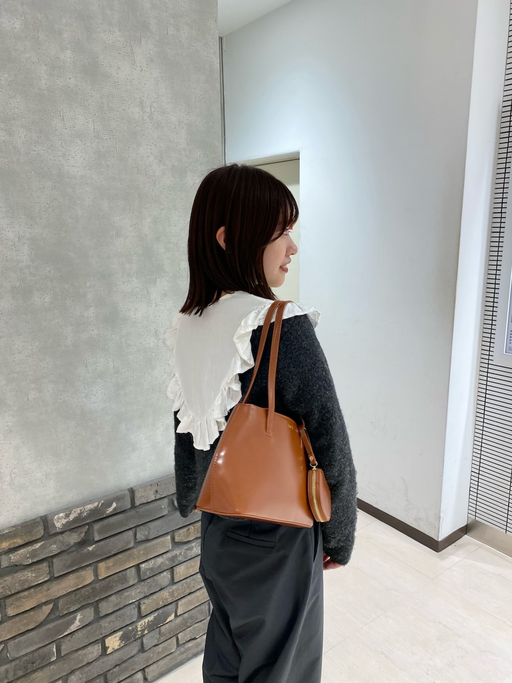 グレー系のカーディガン/ボレロ、ホワイト系のシャツ/ブラウス、ブラウン系のハンドバッグを着用したレディースの冬コーディネートの2枚目の写真