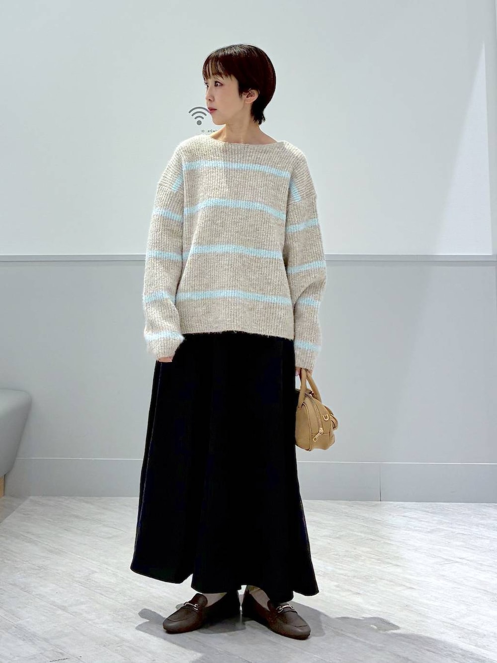 ベージュ系のローファー、グレー系のスカート、ブラウン系のハンドバッグを着用したレディースの秋コーディネートの2枚目の写真