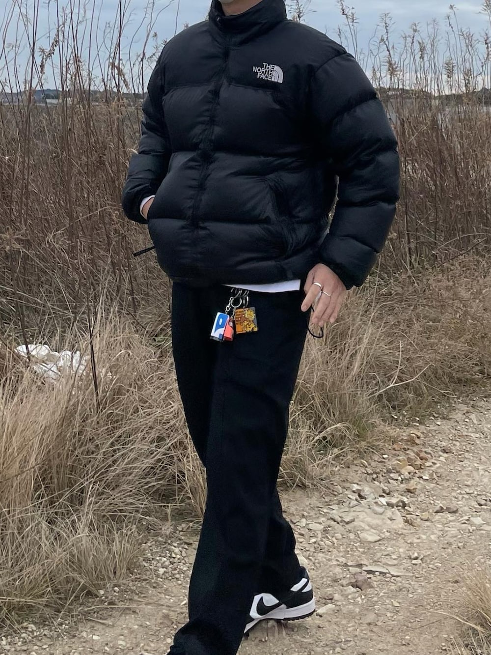 ブラック系のダウンジャケット/コート、ブラック系のスラックス、ホワイト系のスニーカーを着用したメンズの春コーディネートの2枚目の写真