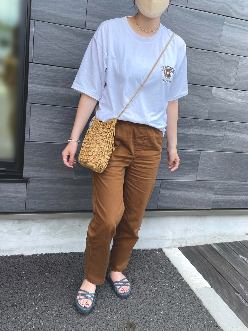 イエロー系のショルダーバッグ、ブラウン系のパンツ、ブルー系のサンダルを着用したレディースの夏コーディネートの2枚目の写真