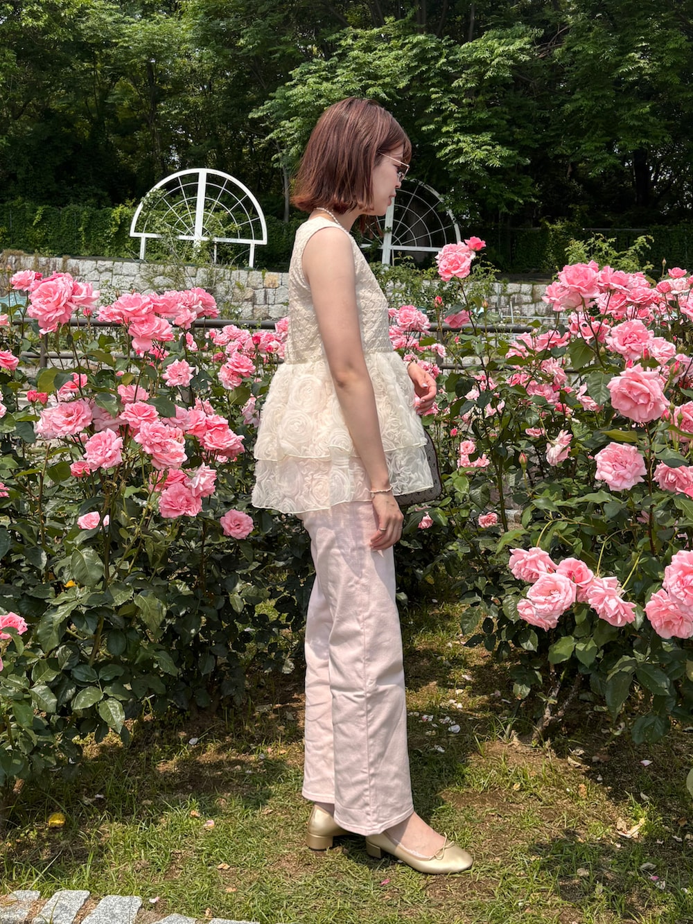 ピンク系のデニムパンツ、ベージュ系のチュニック、ゴールド系のパンプスを着用したレディースの夏コーディネートの2枚目の写真