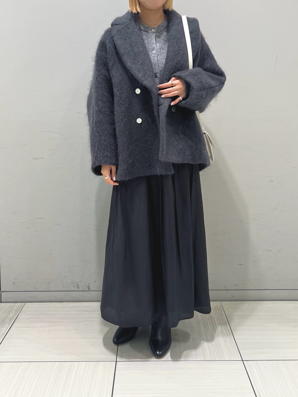 グレー系のピーコート、ブラック系のスカート、ブラック系のブーツを着用したレディースの秋コーディネートの4枚目の写真