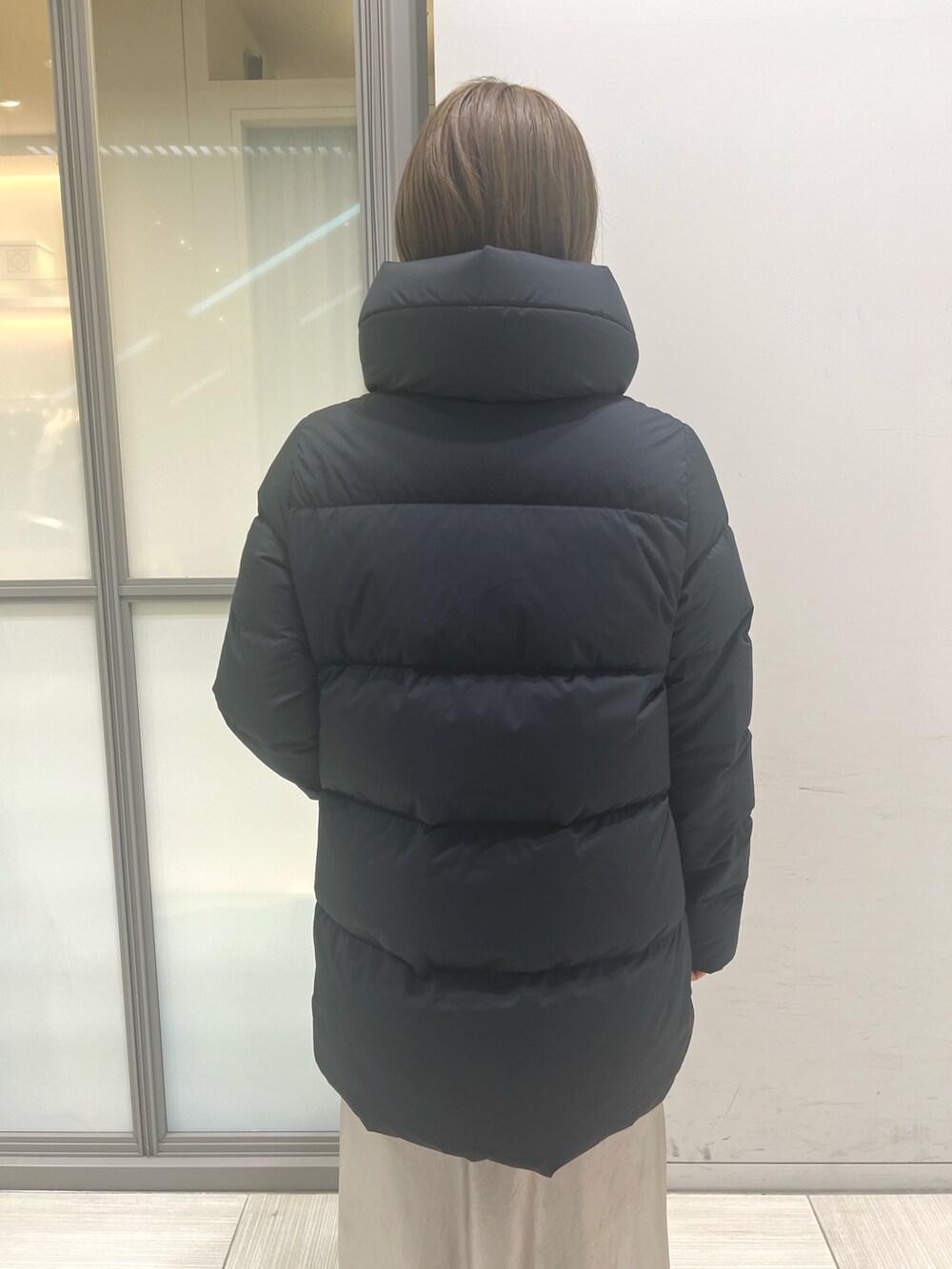 ブルー系のベスト、ベージュ系のスカート、ブラック系のダウンジャケット/コートを着用したレディースの秋コーディネートの3枚目の写真