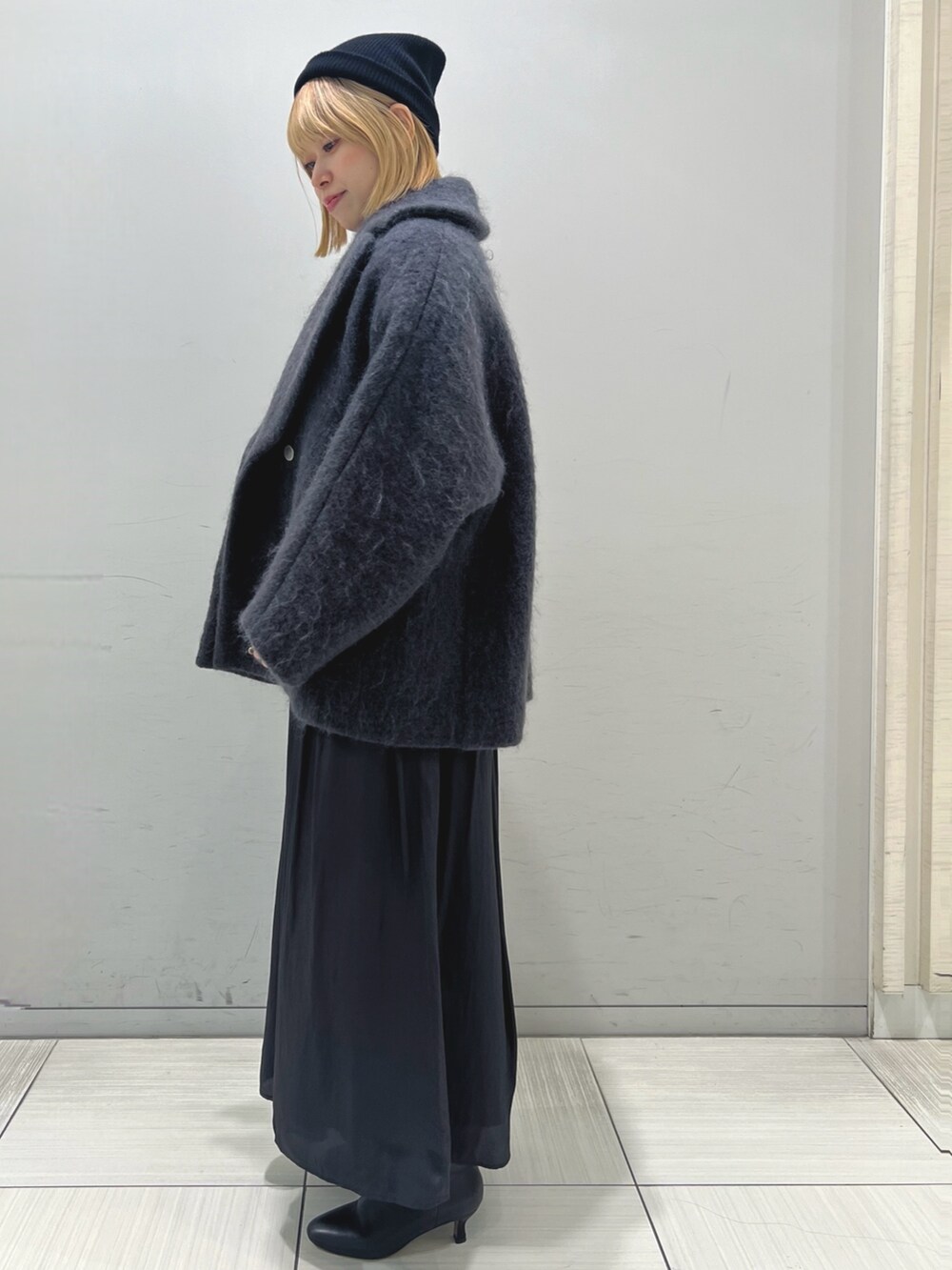 グレー系のピーコート、ブラック系のスカート、ブラック系のブーツを着用したレディースの秋コーディネートの2枚目の写真