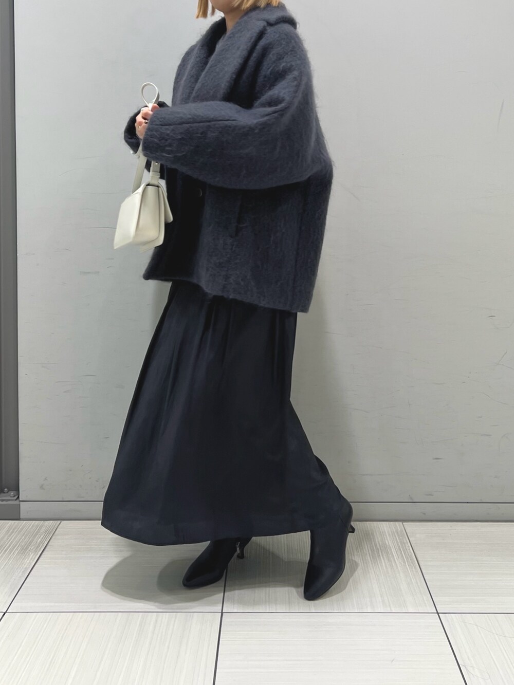 グレー系のピーコート、ブラック系のスカート、ブラック系のブーツを着用したレディースの秋コーディネートの3枚目の写真