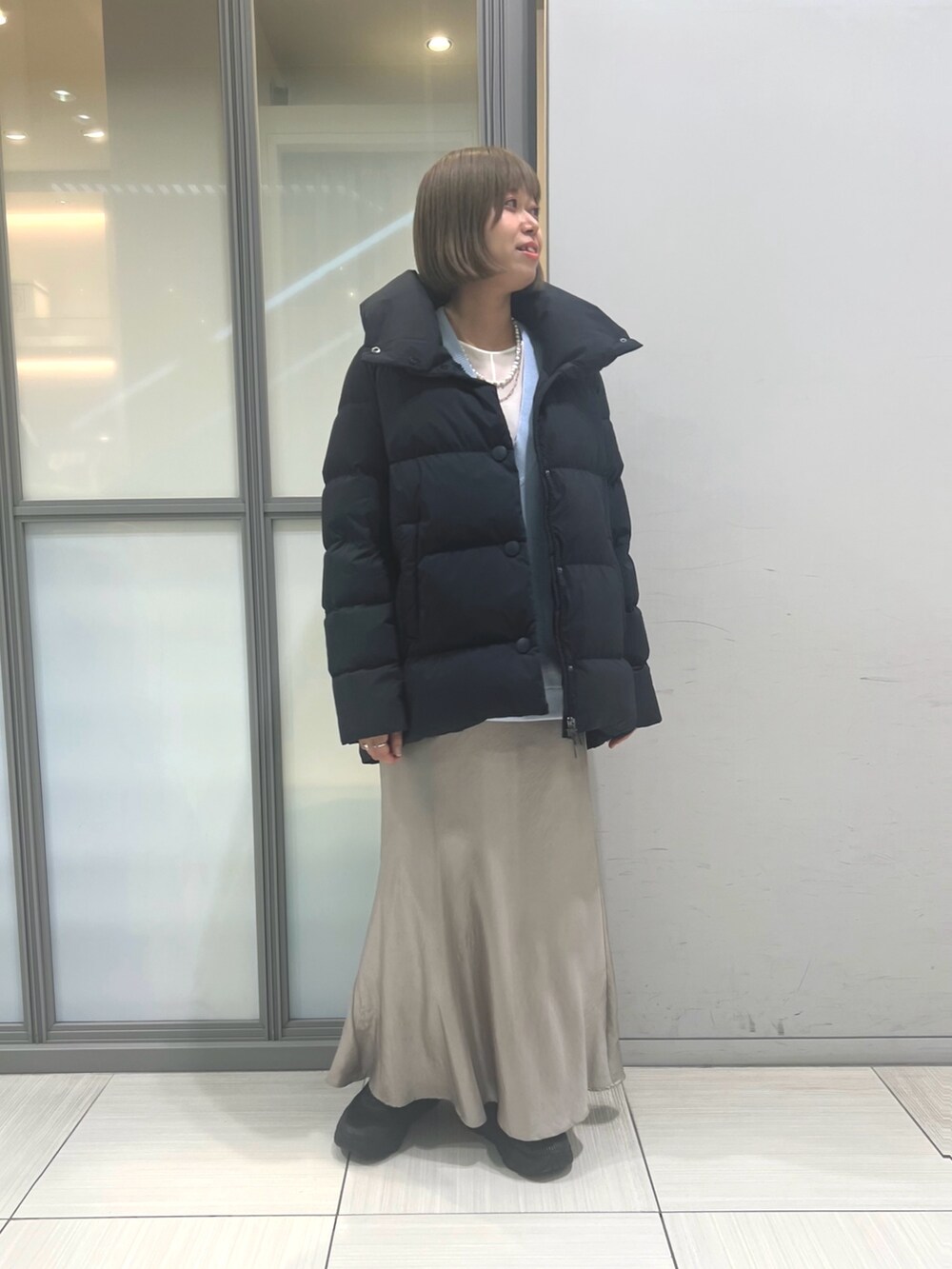 ブルー系のベスト、ベージュ系のスカート、ブラック系のダウンジャケット/コートを着用したレディースの秋コーディネートの2枚目の写真