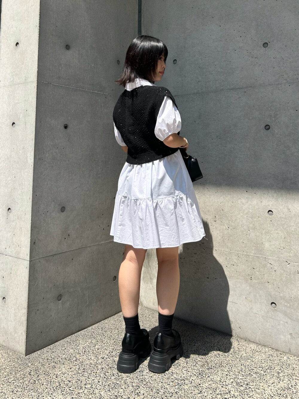 ブラック系のベスト、ブラック系のハンドバッグ、ブラック系のローファーを着用したレディースの夏コーディネートの2枚目の写真