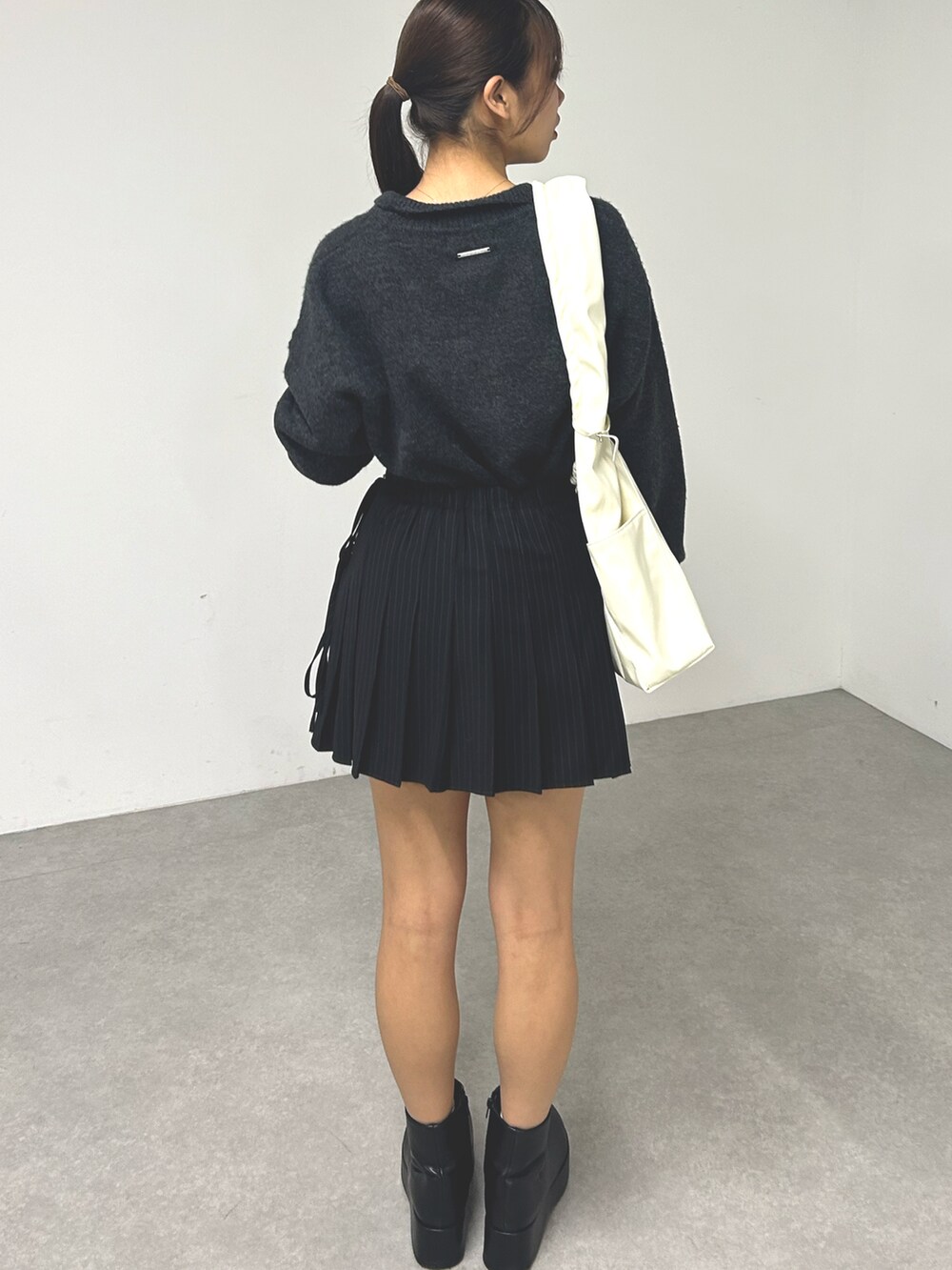 グレー系のニット/セーター、ブラック系のスカート、ホワイト系のハンドバッグを着用したレディースの秋コーディネートの2枚目の写真