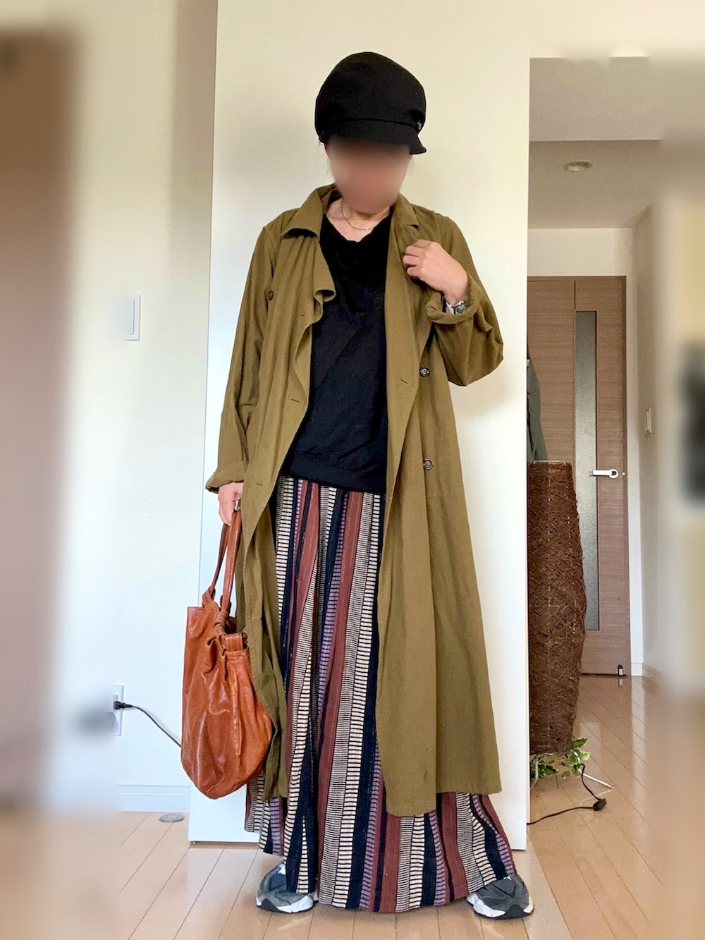 ブラック系のスニーカー、ブラウン系のスカート、グリーン系のトレンチコートを着用したレディースの秋コーディネートの2枚目の写真