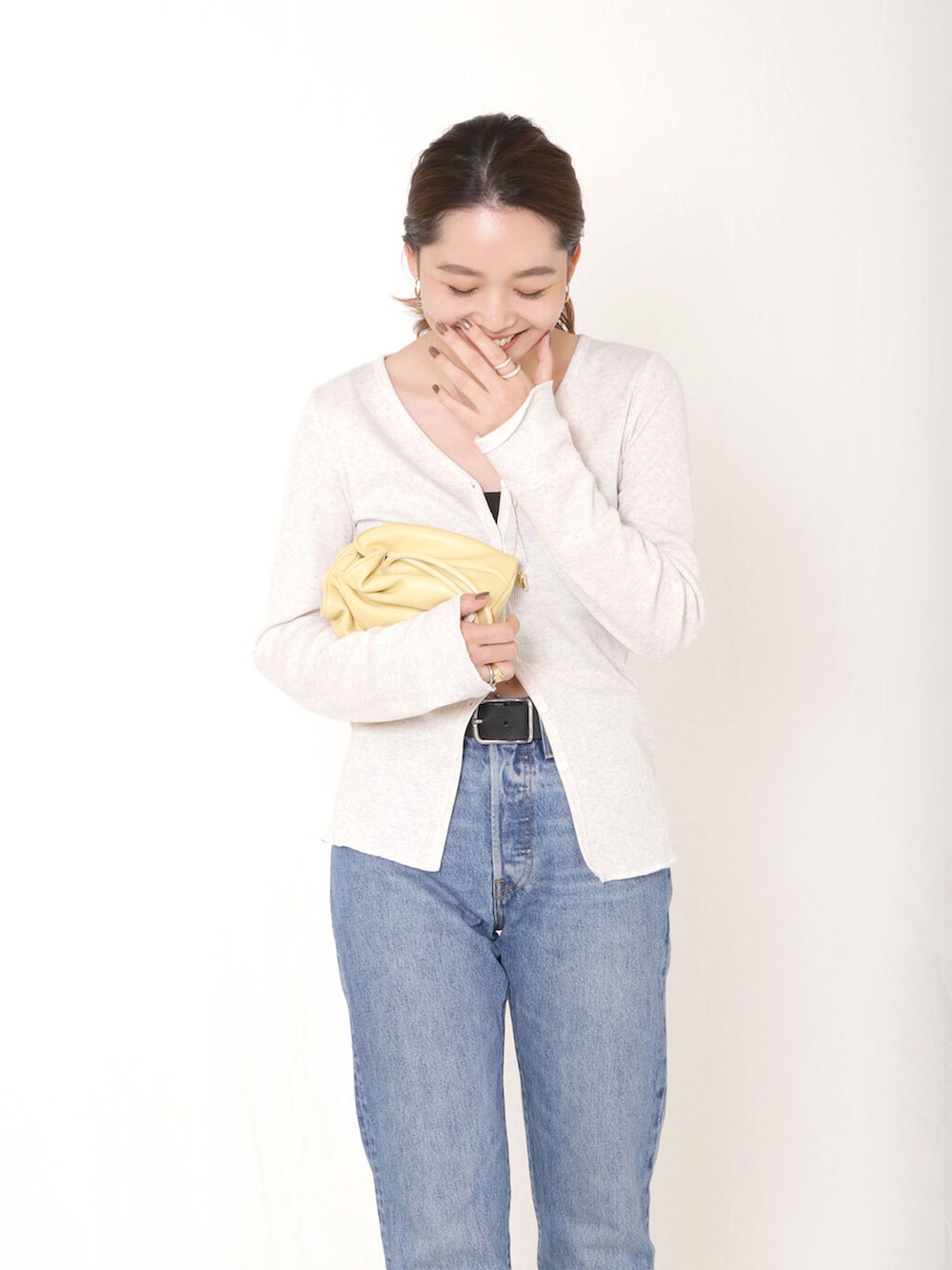 イエロー系のクラッチバッグ、ブルー系のデニムパンツ、ブラック系のブーツを着用したレディースの秋コーディネートの3枚目の写真