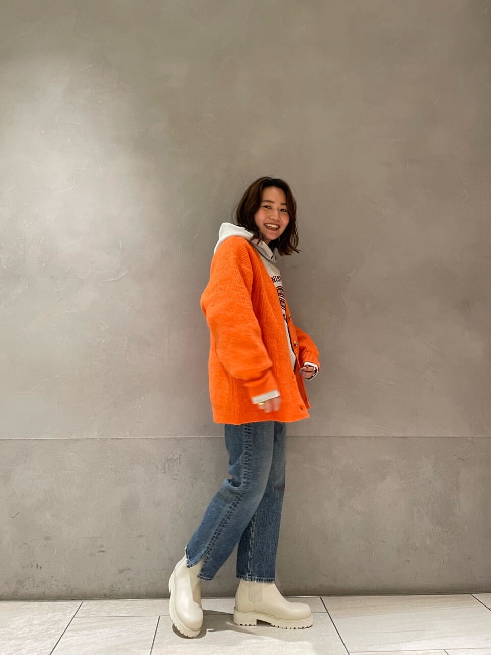 ブルー系のデニムパンツ、グレー系のパーカー、オレンジ系のカーディガン/ボレロを着用したレディースの冬コーディネートの2枚目の写真